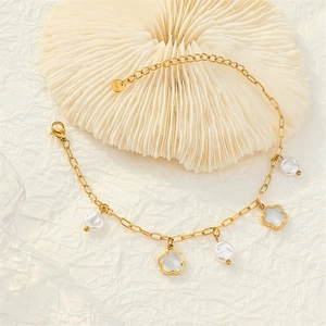 Gold stainless steel chain anklet with white floral charms and pearls on a white plate