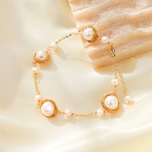 Detailed macro of gold flower pearl bracelet with lobster clasp on silk fabric