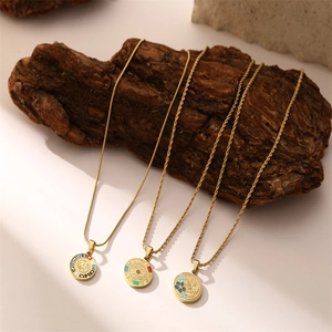 Three gold stainless steel zodiac and floral pendant necklaces displayed on tree bark