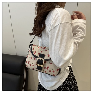 Vue latérale du sac bandoulière en toile à motif cerises avec bordures en cuir noir