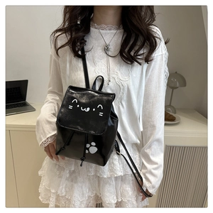 Détail d'un mini sac à dos noir avec motif chat mignon porté par un mannequin en robe blanche