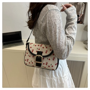 Détail du sac bandoulière en toile avec imprimé cerise, garniture en cuir noir et boucle