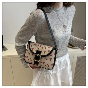 Femme portant un sac bandoulière en toile beige à motifs cerises et finitions en cuir