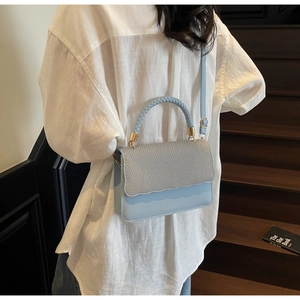 Détails du tissage ondulé et boucles dorées sur un sac à bandoulière bleu clair chic