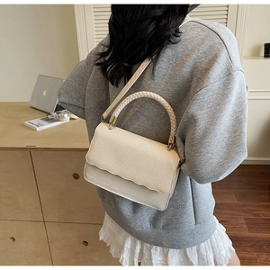 Détail d'un sac à bandoulière crème avec rabat tissé et bordure ondulée sur modèle