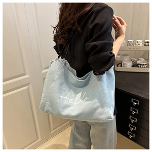 Close-up of light blue denim tote bag featuring white Hello embroidery and black straps