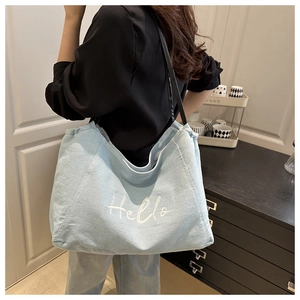Detailed view of light blue denim tote bag with Hello embroidery and black leather strap