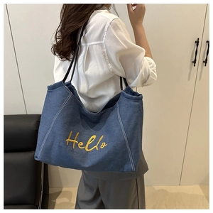 Detail of blue denim tote bag with yellow Hello embroidery and black shoulder strap