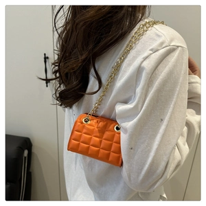 Gros plan du sac matelassé orange avec chaîne dorée porté sur des vêtements blancs