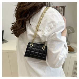Détail du sac matelassé noir à chaîne dorée porté sur une chemise blanche