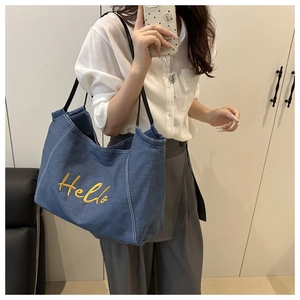 Detailed embroidery of yellow Hello text on a blue denim canvas tote bag with contrast stitching