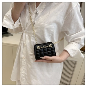 Détail d'un sac à chaîne matelassé noir porté en bandoulière sur une chemise blanche