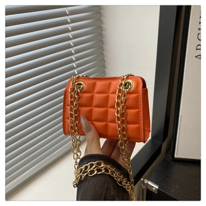 Detail of orange quilted mini bag featuring thick gold chain strap and textured faux leather