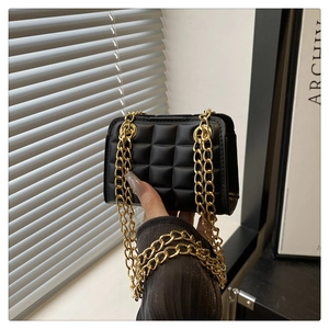 Detail of black quilted square bag with gold chain strap in a hand-held studio shot