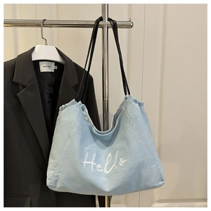 Detail of light blue canvas tote bag with Hello embroidery and black leather handles