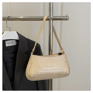 Close-up of cream baguette bag with crocodile texture hanging on a metal hanger