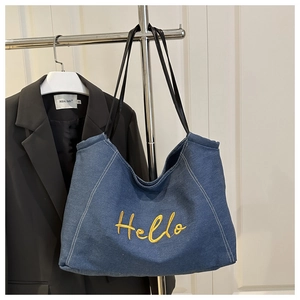Detail of blue denim tote bag with yellow Hello embroidery and black leather straps