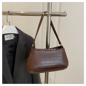 Detail of dark brown crocodile embossed baguette bag hanging on a minimalist steel rod