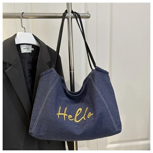 Detail of blue denim tote bag with yellow Hello embroidery and black leather strap
