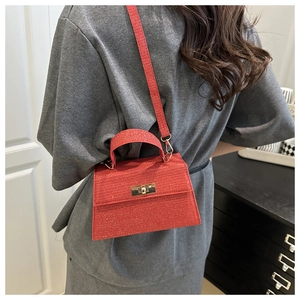 Detail view of red glittery trapezoid handbag featuring gold twist-lock and top handle