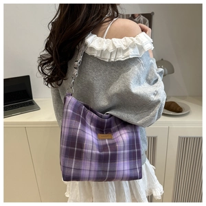 Detail of purple plaid tote bag with wide strap and brown leather brand label