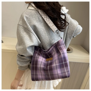 Detail of purple checkered canvas tote bag with wide woven strap and fashion leather tag