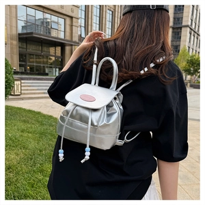 Mini metallic silver backpack with drawstring detail on a model's back in a city park