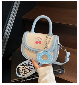 Detail of light blue and cream saddle bag with cherry print and donut pendant charm