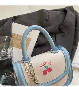Detail of a chic cream and blue crossbody bag with cherry prints and silver chain strap