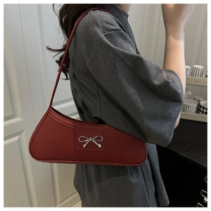 Detail of red faux leather underarm bag with silver bow buckle on model shoulder