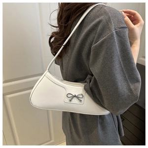 Close-up of a white underarm bag featuring a metallic silver bow on matte leather surface