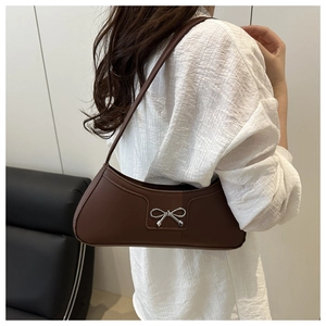 Brown vintage baguette bag with silver metal bow detail shown on shoulder by model