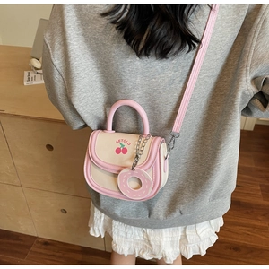 Detail of cream saddle bag with pink trim, cherry print and doughnut charm on crossbody strap