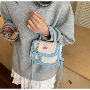 Detail of macaron blue saddle bag featuring cherry print and donut charm accessory