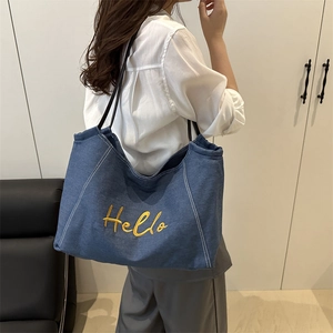Blue denim tote bag with Hello embroidery and black leather straps on a female model