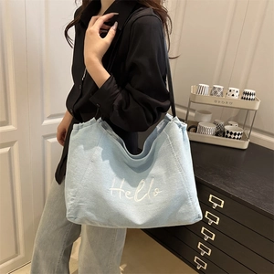 Light blue denim tote bag with Hello embroidery shown on a model in a modern interior