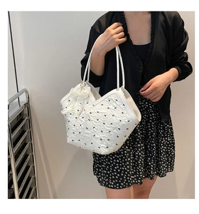 Detail of white pleated shoulder bag with black bow prints and a large pearl accessory