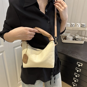Chic pleated cream underarm bag with brown handles, shown worn in a stylish indoor setting