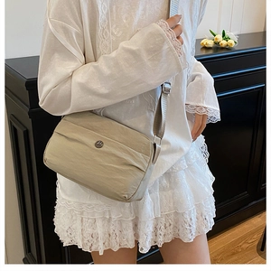 Detail of beige nylon crossbody bag with wide strap and metallic logo on a model