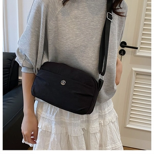 Detail of adjustable wide shoulder strap and silver M logo on black nylon crossbody bag