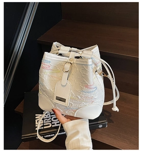 Detail of white leather bucket bag featuring embossed texture and rainbow wavy stitching