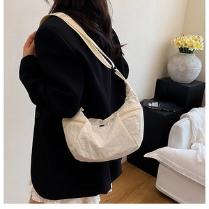 Dettaglio della trama del tessuto pieghettato e della forma a mezzaluna della borsa beige