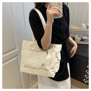 Detail of cream nylon tote bag with wide strap and lucky charm patch in home setting