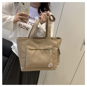 Detail of khaki nylon tote bag showing front zipper pocket and good luck patch