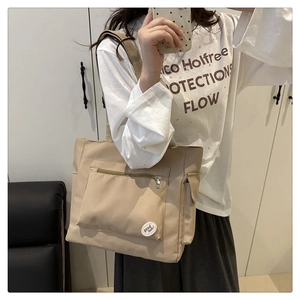 Detail of khaki nylon tote bag featuring front zip pocket and round good luck patch