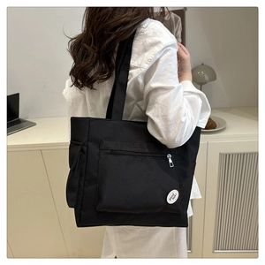 Detail view of a large black canvas tote bag showing the front zipper pocket and round label