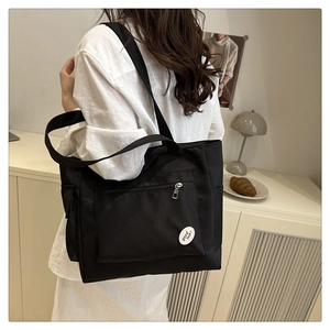 Detail of black canvas tote bag showing front zipper pocket and good luck embroidery