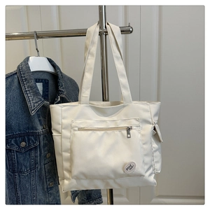 Detail of white canvas tote bag with zippered front pocket and good luck badge ornament