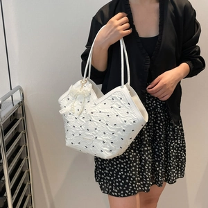 White textured tote bag with blue bow prints and pearl lace charm on a model