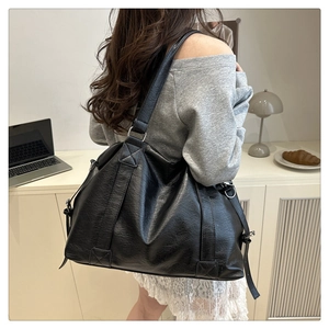 Detail of black pebbled leather tote bag with wide strap and metallic rings on shoulder